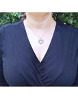 Woman wearing a 14K gold necklace with a heart-shaped emerald pendant.