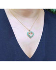 14K gold heart-shaped pendant necklace with vibrant green Colombian emeralds on a woman's chest.