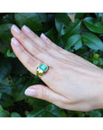 Hand wearing a gold ring for men with a natural emerald against a leafy background.