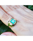 A men's gold ring with a bezel set natural emerald on a hand against a natural background.