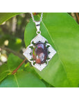 Silver pendant with a black opal on a green leaf background.