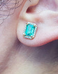 Close-up of an emerald gemstone earring with halo diamond on a person's ear.