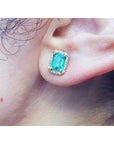 Close-up of an emerald gemstone earring with halo diamond on a person's ear.