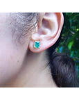 Emerald stud earring with diamond halo in 14k yellow gold on an ear.