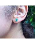 Emerald stud earring with diamond halo in 14k yellow gold on an ear.