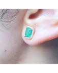 Emerald stud earring with diamond halo in 14k yellow gold on an ear.