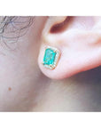 Emerald stud earring with diamond halo in 14k yellow gold on an ear.