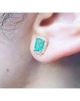 Emerald stud earring with diamond halo in 14k yellow gold on an ear.