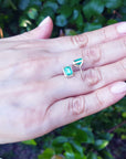 Yellow gold earrings with natural emeralds held in a hand against a blurred green background