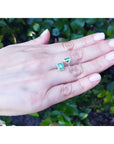 Emerald stud earrings with diamond halo in 14k yellow gold, displayed on a hand.