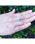 Emerald stud earrings with diamond halo in 14k yellow gold, displayed on a hand.