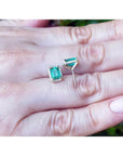 Emerald stud earrings with diamond halo in 14k yellow gold, displayed on a hand.