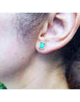 Emerald stud earring with diamond halo in 14k yellow gold, worn on an ear.