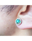 Close-up of an ear wearing halo diamond emerald stud earring.