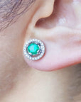 Close-up of an ear wearing a natural halo diamond emerald stud earring,