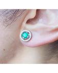 1.06 ct deep bluish-green Colombian emerald stud earring with diamond halo and secure screw back on an ear.