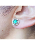 1.06 ct deep bluish-green Colombian emerald stud earring with diamond halo and secure screw back on an ear.