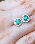 Pair of emerald stud earrings on a hand.
