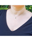 Minimalist 14K yellow gold necklace with a round cut green emerald and small diamond accents, worn on a woman.