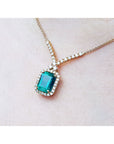 14K yellow gold halo necklace with a rectangular bluish-deep green emerald and natural diamonds.