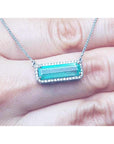 Woman's hand holding a Muzo Colombia Emerald necklace east west orientation encircle by halo diamonds