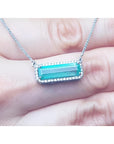 18K white gold necklace with a rectangular Colombian emerald and diamond halo, East-West design.