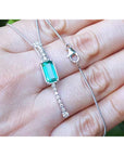 Lariat white gold necklace with a natural emerald gemstone held in a hand against a blurred background