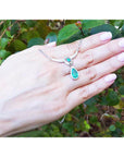 Hand displaying an authentic Colombian emerald necklace May birthstone pear-shaped against a green leafy background