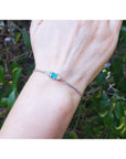 Hand wearing a bracelet with a colombian emerald against a natural background.