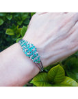 Emerald and diamonds bangle bracelet on a wrist with a green leafy background.