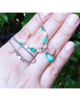 Hand holding White gold 14k Emerald necklaces pear shaped wheat style chain against a blurred green background