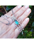 Marquise Colombian emerald and diamond necklace in 14K white gold, held in a hand.