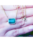 Emerald-cut Colombian emerald solitaire necklace in 18K yellow gold, held in a hand.