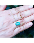 Deep green emerald solitaire necklace in 18K yellow gold, held in a hand.