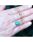 Deep green emerald solitaire necklace in 18K yellow gold, held in a hand.