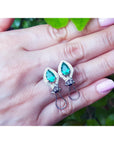 Teardrop-shaped pear-cut emerald earrings held in a hand with pink nail polish.