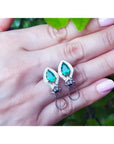14K white gold clip/post earrings with pear-shaped Colombian emeralds and diamond accents on a hand.