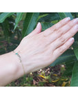 Emerald Love Bracelet in 14K white and yellow gold with a round cut green emerald, worn on a hand.