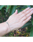 Emerald Love Bracelet in 14K white and yellow gold with a round cut green emerald, worn on a hand.