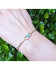 14K yellow gold bracelet with a square emerald-cut Colombian emerald on a woman's wrist.