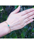 Woman's hand wearing a 14K yellow gold paper clip bracelet with a rectangular emerald and diamonds.