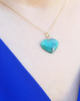 Hand carved emerald heart-shaped pendant on a gold chain worn by a person's neck.