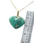 A cabochon hand carved emerald heart-shaped pendant on a gold chain with a ruler for scale.