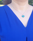 Person wearing a blue dress with a heart-shaped cabochon heart emerald pendant necklace outdoors.