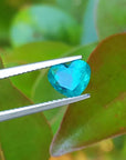 1.26 ct. vibrant bluish-green heart-cut Colombian emerald held by tweezers.