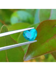 1.26 ct. vibrant bluish-green heart-cut Colombian emerald held by tweezers.