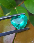 2.54 carat GIA certified heart cut Colombian emerald, sparkling bluish-green, held by tweezers.