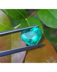 2.54 carat GIA certified heart cut Colombian emerald, sparkling bluish-green, held by tweezers.