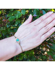 Hand wearing a 14K yellow gold bracelet with a heart-shaped Colombian emerald and diamonds.