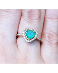 Heart-shaped emerald ring with halo diamond made of 14k yellow gold on a finger.
